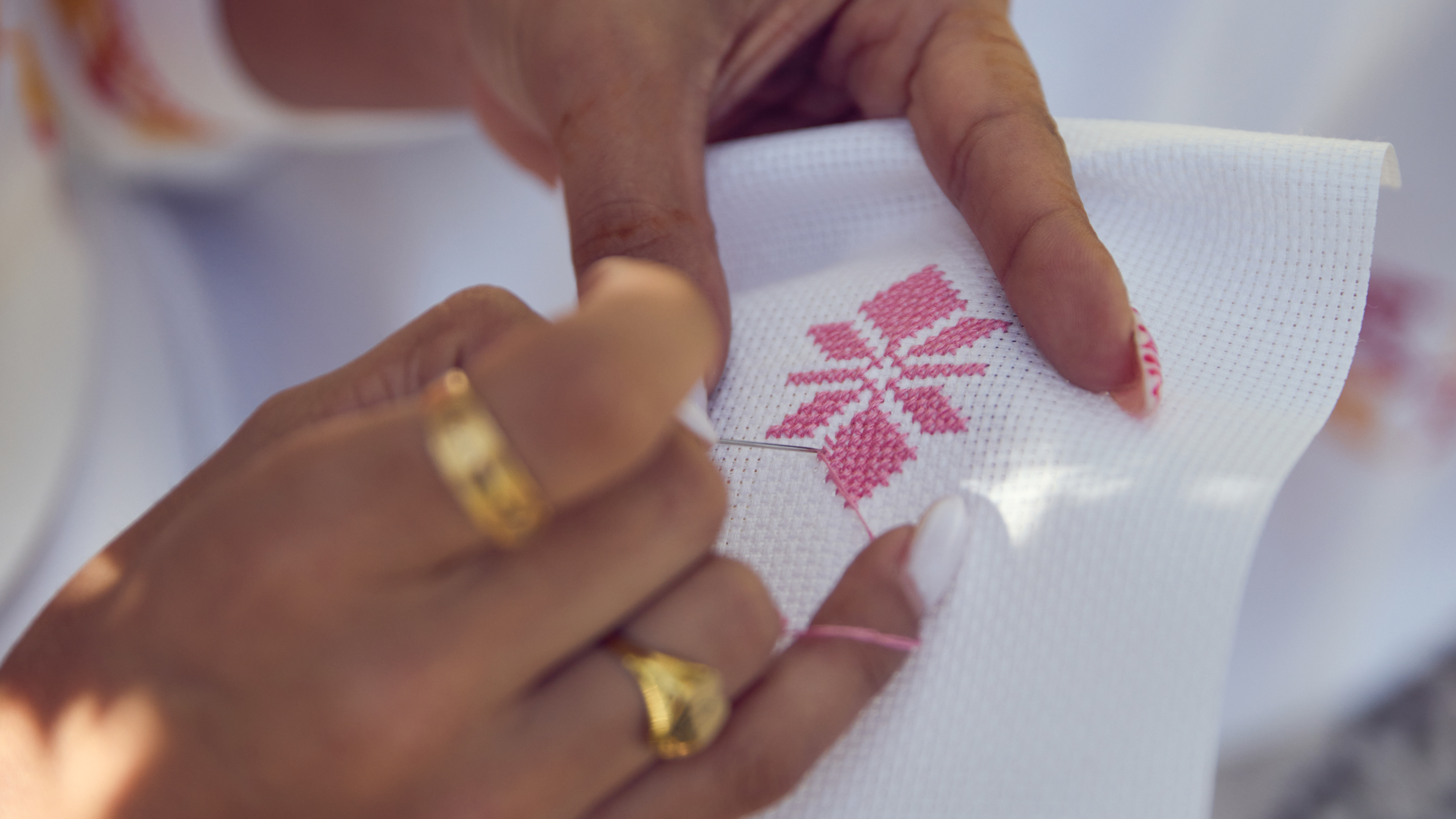 Close-up of hands with rings stitching a snowflake design on fabric.