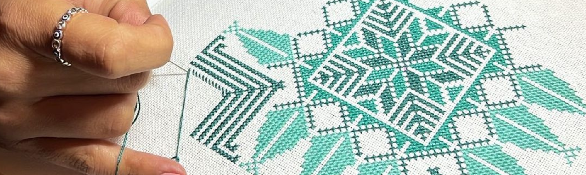 Photo of dark green and light green tatreez pattern stitched onto white canvas 